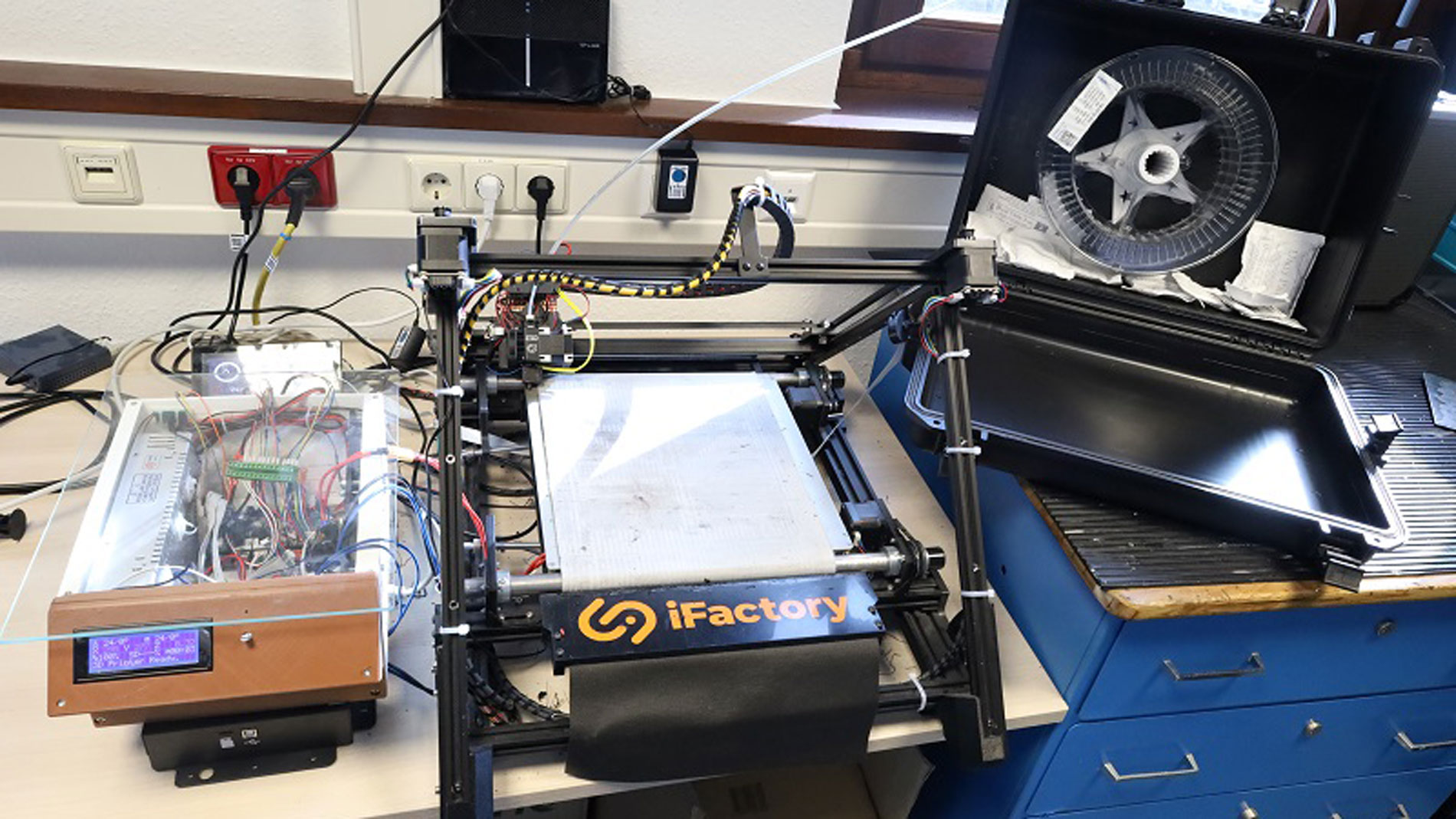 A lot of expertise has gone into modifying this iFactory belt printer. On the right, an air-tight case has been opened to access the filament inside. Image: Thomas Masuch